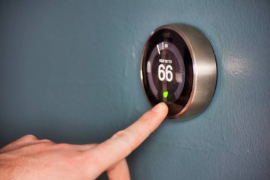 Hand operating smart thermostat to save money clipart
