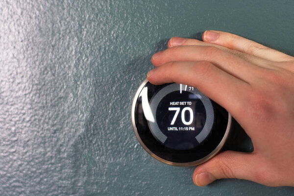 Nest smart home being adjusted by hand in blue wall. Isolated product photo in use