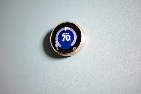 smart home thermostat isolated on blue wall. Room for copy and writing. Green tech heating and cooling