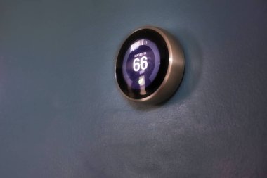 Evde 66 derece gösteren akıllı termostat. Yeşil teknolojiyle para biriktirmek için mavi duvardaki termostatın ısı ayarlaması.