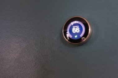 Evde 66 derece gösteren akıllı termostat. Yeşil teknolojiyle para biriktirmek için mavi duvardaki termostatın ısı ayarlaması.