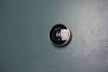 Evde 66 derece gösteren akıllı termostat. Yeşil teknolojiyle para biriktirmek için mavi duvardaki termostatın ısı ayarlaması.