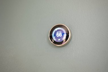 Evde 66 derece gösteren akıllı termostat. Yeşil teknolojiyle para biriktirmek için mavi duvardaki termostatın ısı ayarlaması.