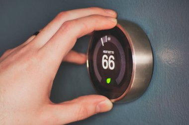 Hand operating smart thermostat to save money. Hand making adjustments by turning knob. Smart home. clipart