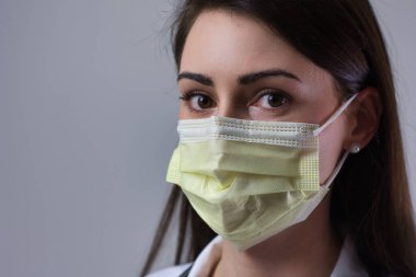 Female hospital worker wearing yellow face mask. Eyes visible over cover. Isolated on grey background. clipart