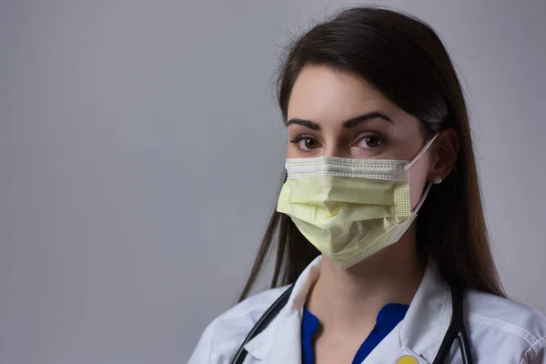 Female healthcare worker wearing mask isolated on grey background. Space for copy or text. Wearing stethoscope and white coat.