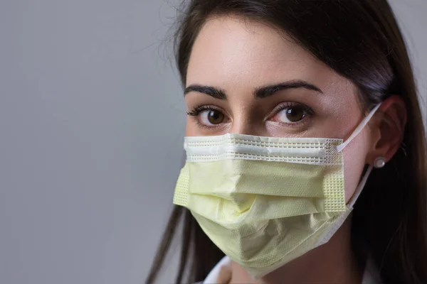 Gri bir geçmişi olan maskeli bir tıp uzmanı. Boynuna steteskop takmış bir doktor. Kadın doktor.