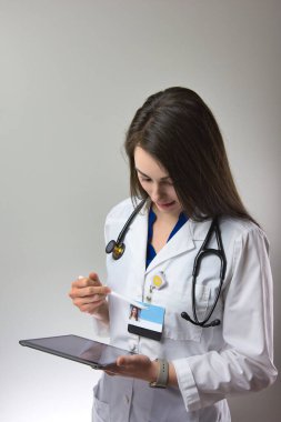 Dark haired woman making note in patient chart. Female healthcare worker with stethoscope making notes clipart