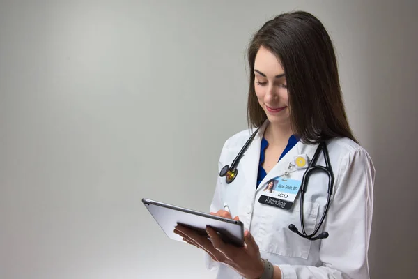 Tablet ve steteskop kullanan bir tıp uzmanı hasta tablosu üzerinde notlar tutuyor.