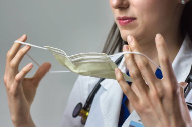 Kadın sağlık uzmanı Coronavirus 'tan korunmak için uygun bir maske takıyor. Yakın bir kadın sağlık çalışanı gri arka plana güvenlik ekipmanı takıyor.