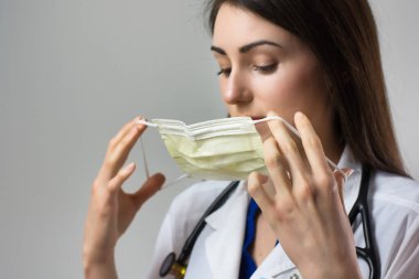Kadın sağlık uzmanı Coronavirus 'tan korunmak için uygun bir maske takıyor. Yakın bir kadın sağlık çalışanı gri arka plana güvenlik ekipmanı takıyor.