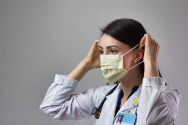 Kadın sağlık uzmanı Coronavirus 'tan korunmak için uygun bir maske takıyor. Yakın bir kadın sağlık çalışanı gri arka plana güvenlik ekipmanı takıyor.