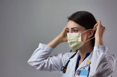 Kadın sağlık uzmanı Coronavirus 'tan korunmak için uygun bir maske takıyor. Yakın bir kadın sağlık çalışanı gri arka plana güvenlik ekipmanı takıyor.