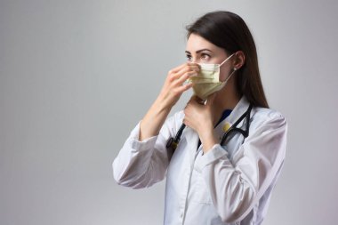 Kadın sağlık uzmanı Coronavirus 'tan korunmak için uygun bir maske takıyor. Yakın bir kadın sağlık çalışanı gri arka plana güvenlik ekipmanı takıyor.