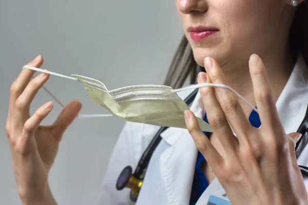 Kadın sağlık uzmanı Coronavirus 'tan korunmak için uygun bir maske takıyor. Yakın bir kadın sağlık çalışanı gri arka plana güvenlik ekipmanı takıyor.