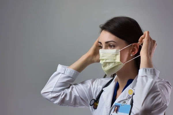 Kadın sağlık uzmanı Coronavirus 'tan korunmak için uygun bir maske takıyor. Yakın bir kadın sağlık çalışanı gri arka plana güvenlik ekipmanı takıyor.