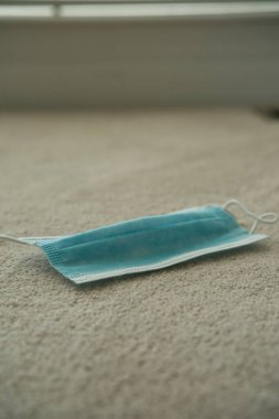 Yüz maskesi halı zemininde izole edilmiş. Mavi maske yüzünü, burnunu ve ağzını kovid 19 koronavirüsten korumak için.