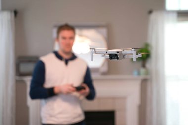Uzaktan kumandalı uçak arka planda pilotla içeri uçuyor. Amatör İHA uçuşu. Soğuk bir günde evde dron uçuran bir kazak giyen kullanıcı. Beyaz İHA içeri uçuyor.