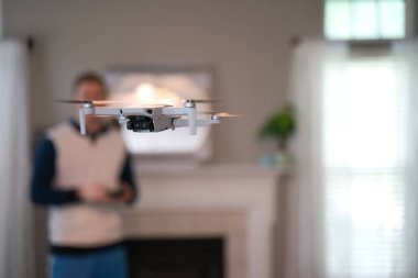 Uzaktan kumandalı uçak arka planda pilotla içeri uçuyor. Amatör İHA uçuşu. Soğuk bir günde evde dron uçuran bir kazak giyen kullanıcı. Beyaz İHA içeri uçuyor.