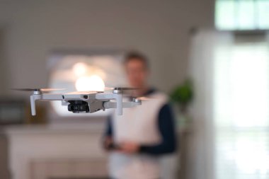 Uzaktan kumandalı uçak arka planda pilotla içeri uçuyor. Amatör İHA uçuşu. Soğuk bir günde evde dron uçuran bir kazak giyen kullanıcı. Beyaz İHA içeri uçuyor.