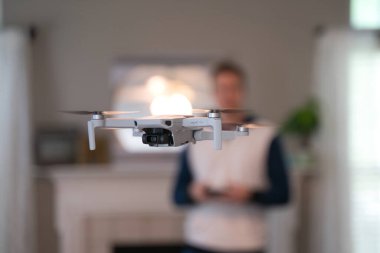 Uzaktan kumandalı uçak arka planda pilotla içeri uçuyor. Amatör İHA uçuşu. Soğuk bir günde evde dron uçuran bir kazak giyen kullanıcı. Beyaz İHA içeri uçuyor.