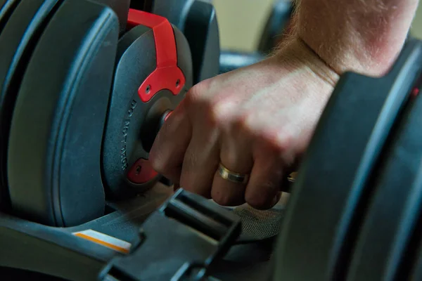 Hand gripping adjustable dumbbells for working out at home. male hand with ring visible.