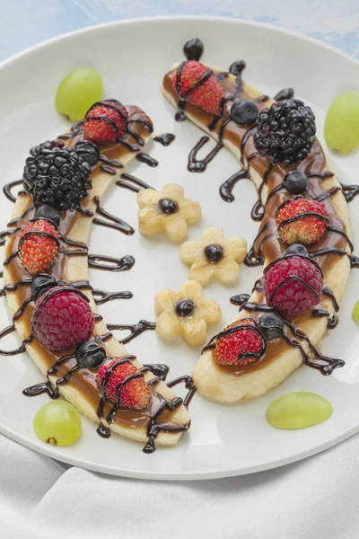 Sobremesa de uma fatia de banana com bagas e cobertura de chocolate — Fotografia de Stock