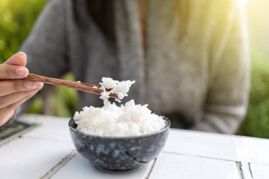 Asyalı kadınlar ellerinde yemek çubuklarıyla pişirilmiş yasemin kaseleri tutuyorlar. Gri bir kazak giyiyor..