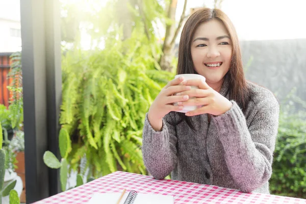 Asian woman relaxing on table with hot coffee at the garden in the house.