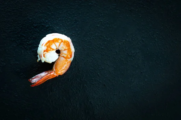 Boiled shrimps on a black background. Dark texture.