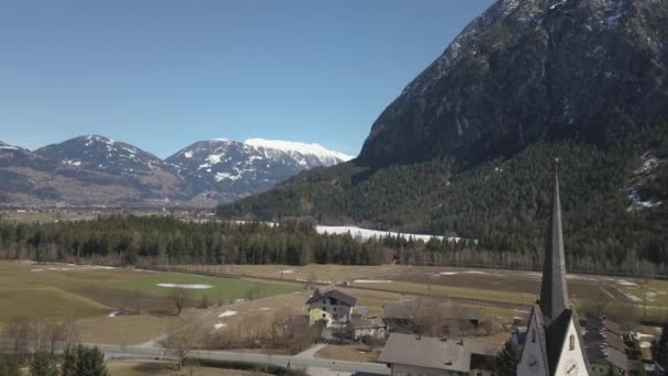 Widok z lotu ptaka na kościół w małym miasteczku pomiędzy potężnymi górami w Alpach — Wideo stockowe