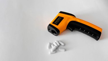 Beyaz arka planda hapların yanında elektronik termometre..