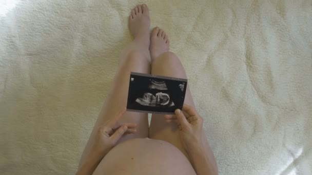 Hamile kadın doğmamış bebeğinin fotoğrafına bakar. — Stok video