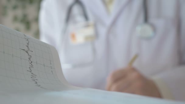 Доктор кардіолог у своєму кабінеті пише результати тестування своїм документам . — стокове відео