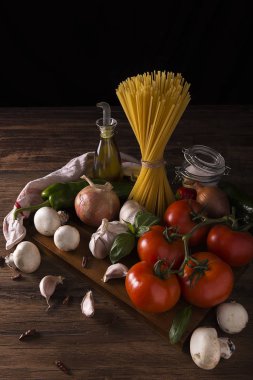 Makarna, domates, sarımsak, soğan, mantar, tuz, zeytinyağı ve ahşap bir masada yeşil biber.