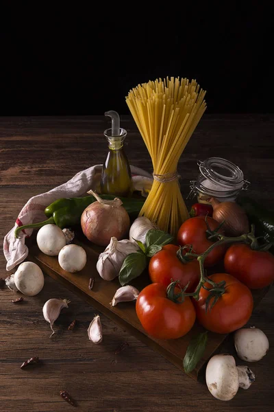 Makarna, domates, sarımsak, soğan, mantar, tuz, zeytinyağı ve ahşap bir masada yeşil biber.