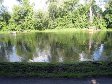 Göl kıyısında güneşli bir gün. Renkli tekneler ve içinde insanlar var.