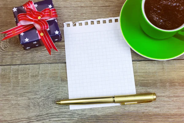 Blank paper with pen, coffee cup and the gift on wood table