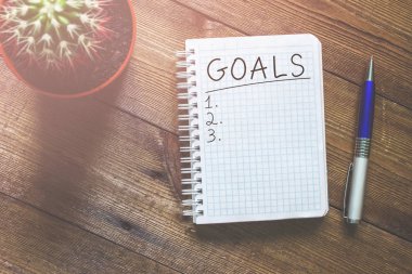 Gol ahşap bir masa üzerinde bir not defteri ve bir kaktüs işleyici ile yazılır