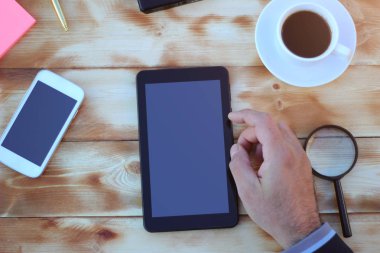 Akıllı telefon, tablet ve bir fincan kahve ile ahşap bir masa üzerinde finansal araçlar