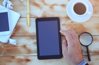 Akıllı telefon, tablet ve bir fincan kahve ile ahşap bir masa üzerinde finansal araçlar