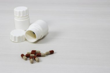 Bir grup renkli ilaç kapsülü arka planda beyaz bir kavanozdan döküldü. Yan görünüş, mesaj için yer. Tıp kavramı.