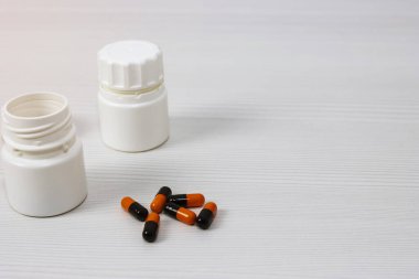 Dağınık siyah-turuncu ilaç kapsüllerinin yanında boş bir kavanoz.