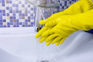 Sarı lastik eldivenli bir kadın ellerini yakından yıkıyor. Temizlik kavramı