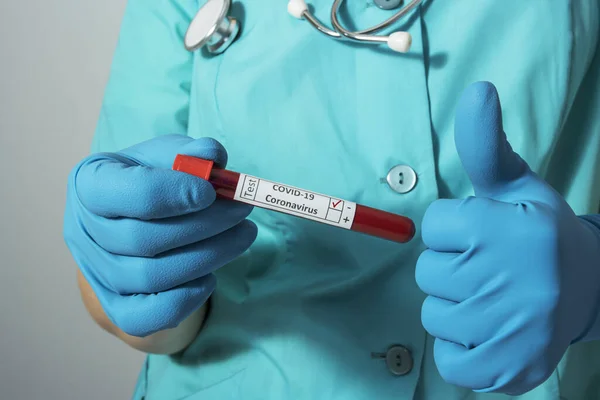 Doctor in a protective suit and blue gloves holds a blood sample in a test tube. The concept of the study of coronavirus