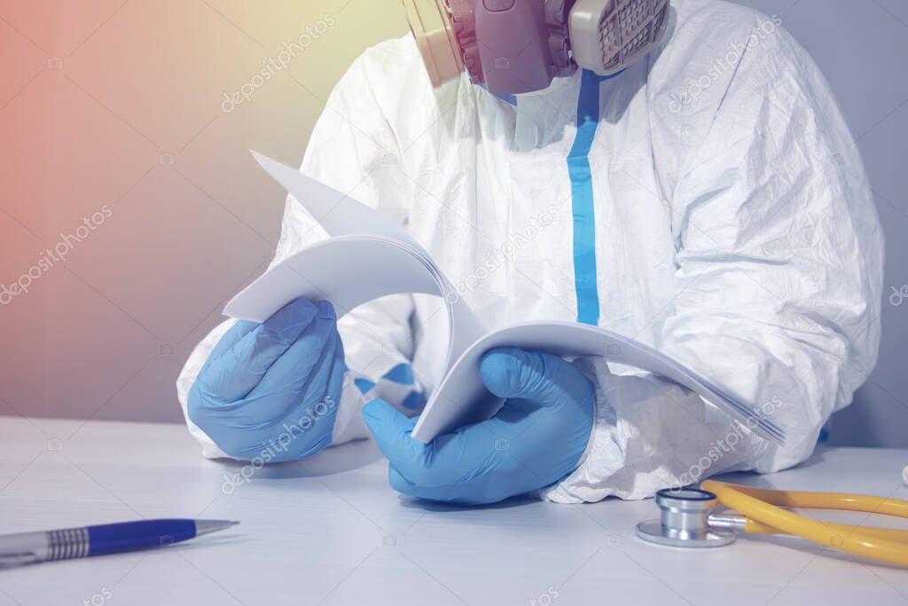 A doctor in a protective biological suit , wearing a respirator and gloves flips through the pages of a notebook