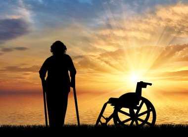 Koltuk değneği deniz günbatımı ve tekerlekli sandalye bir arka plan üzerinde yaşlı bir kadın silüeti