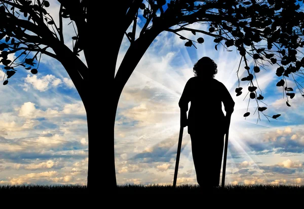 Silhouette di una vecchia donna con le stampelle appoggiate sotto un albero . — Foto Stock
