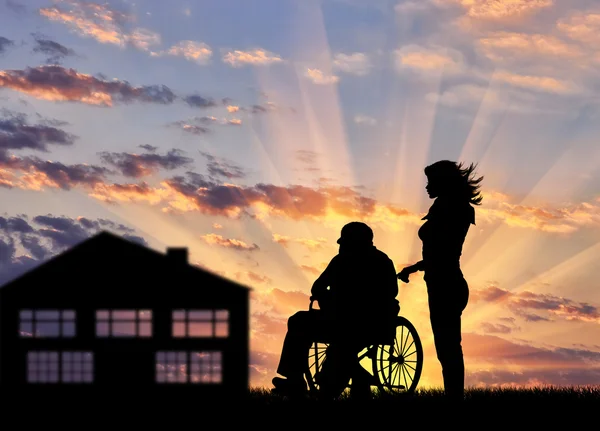 Sziluettjét a nővér a kerekesszék fogyatékkal élő személy gondozása — Stock Fotó