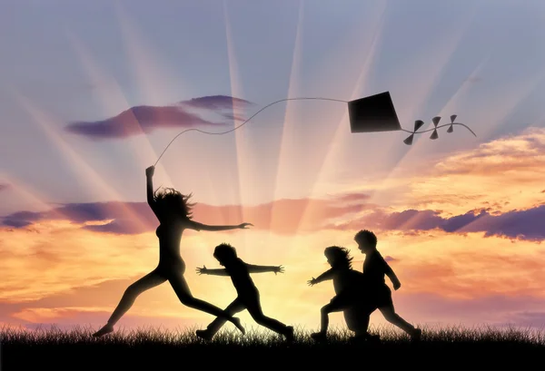Жінка і діти грають з повітряним змієм захід сонця — стокове фото
